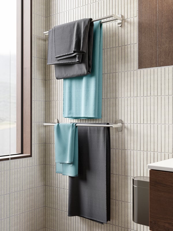 Two anthracite and two blue towels hung neatly on two towel rails against a beige tiled wall.