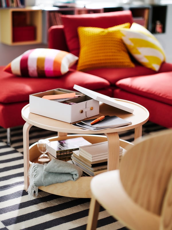 Gemütliches Wohnzimmer mit roten SÖDERHAMN Sitzelementen, die mit bunten gestreiften und gelben SVARTPOPPEL Kissen geschmückt sind. Auf einem BORGEBY Couchtisch aus Holz liegen Bücher und Schreibwaren, darunter befindet sich ein gestreifter Teppich.
