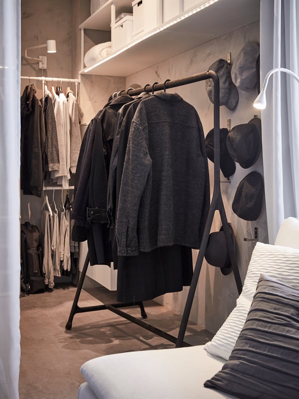 Coats and winter jackets are hanging on a black TURBO clothes rack which is standing against the wall of a bedroom.