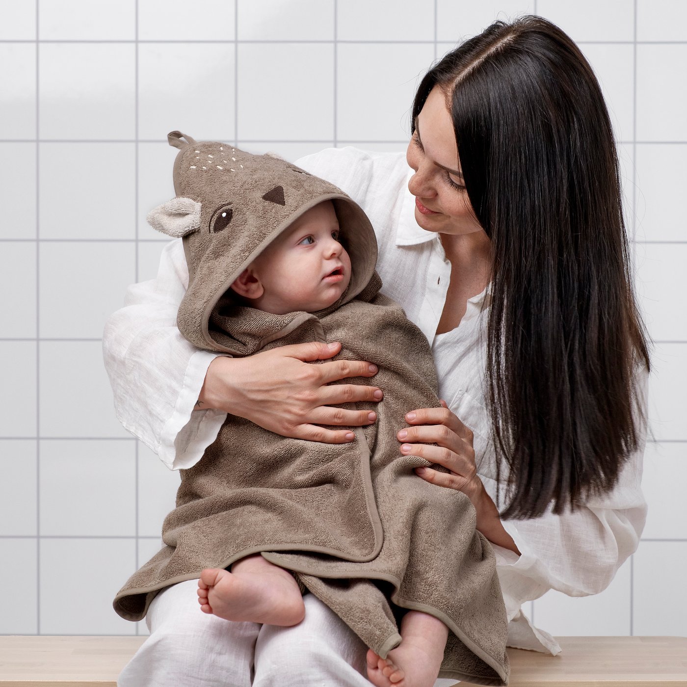 A woman with a baby in a TROLLDOM hooded towel in the bathroom.
