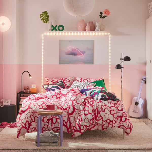 A colourful bedroom features a white and bright pink HÄRLIR duvet cover and pillowcases with a floral pattern on the bed.