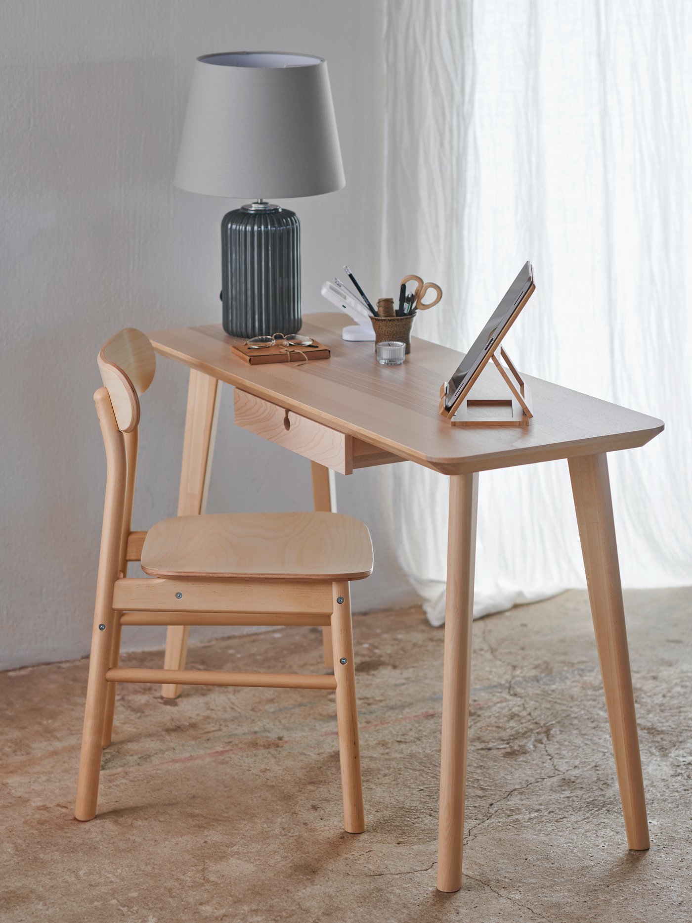 A workstation with a RÖNNINGE chair pulled out from underneath a LISABO table, in a rustic space with concrete floors.