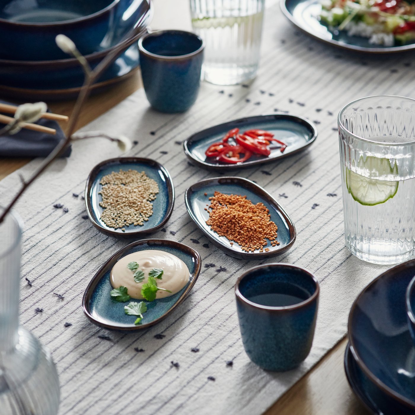 Blue GLADELIG side plates and GLADELIG mugs on a table runner.