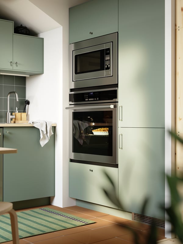 Cuisine aux façades NICKEBO vert-gris équipée d’un four encastrable, d’un four à micro-ondes et d’un ensemble réfrigérateur/congélateur avec façade de même style.