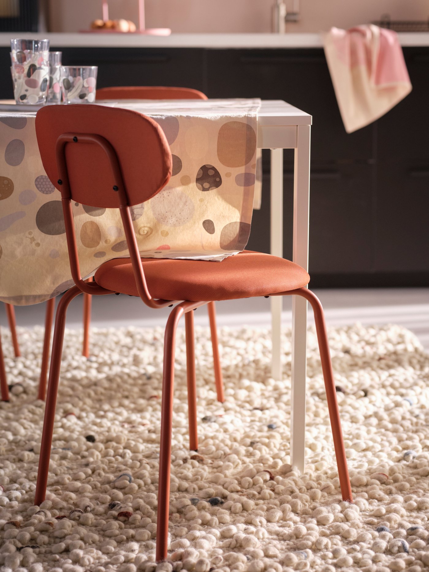 Una silla de comedor ÖSTANÖ rojiza en el costado de una mesa. Debajo de ella hay una alfombra mullida de color beige.