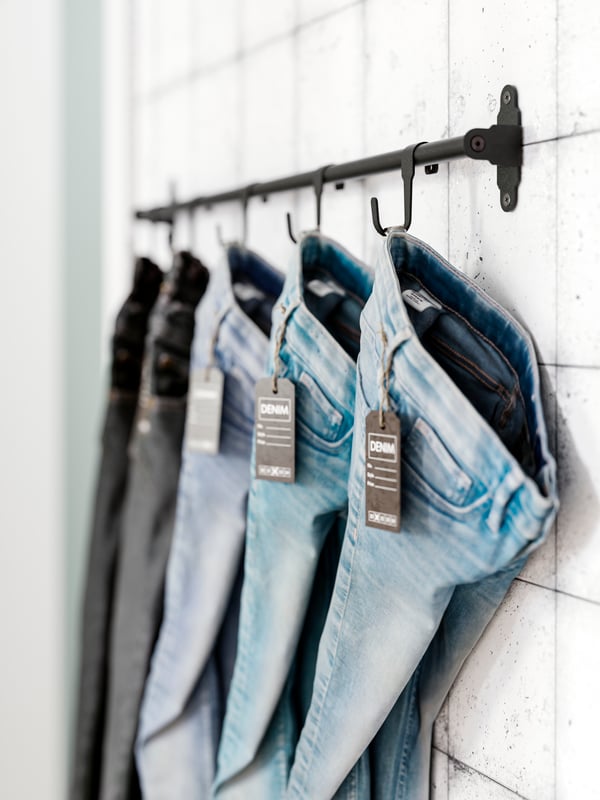 A collection of blue jeans hang from different black HULTARP hooks.