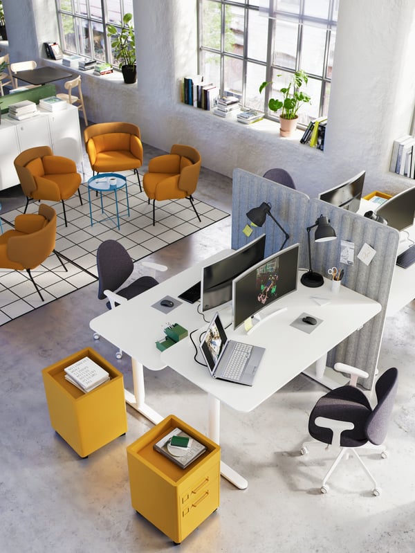 A co-working office with four desks arranged together and an area for lounging with yellow armchairs on checked rugs.