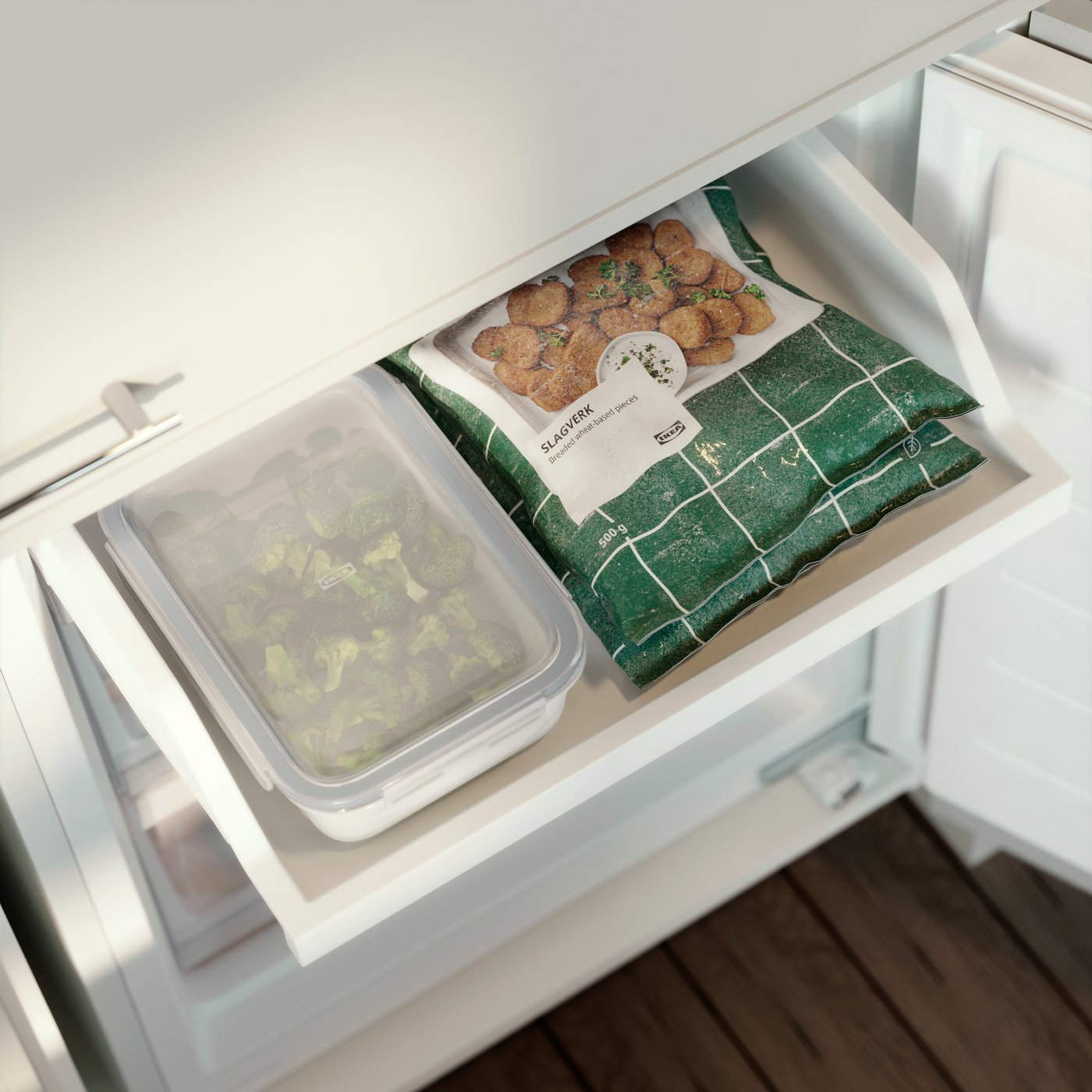 IKEA 365+ food container with broccoli stored in a freezer drawer next to frozen food packages.