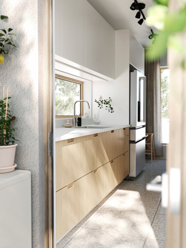 A patio door is open leading into a kitchen with stone floors, FÖRJERED fronts at the bottom and VEDDINGE fronts at the top.