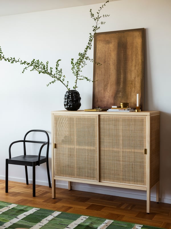 Ein STOCKHOLM 2025 Schiebetürenschrank steht an der Wand. Auf ihm befindet sich eine Vase mit Zweigen. Daneben steht ein Stuhl.