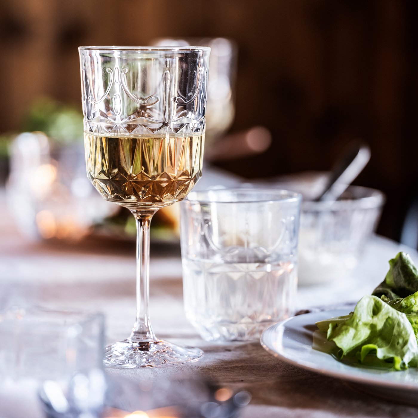 SÄLLSKAPLIG čaša za vino na stolu s tanjirom salate i čašom za vodu.