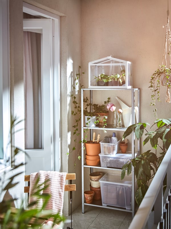 A bright corner of an outdoor balcony with a metal outdoor shelving unit displaying gardening tools, plants and plant pots.