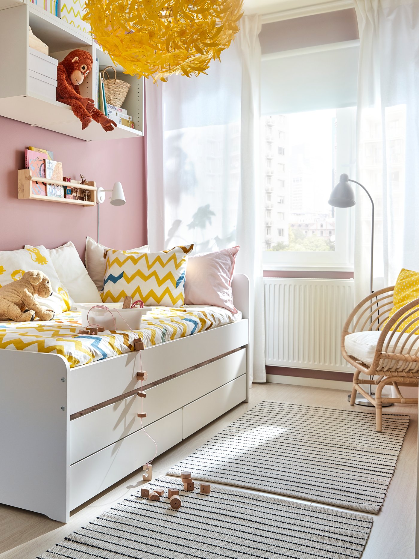 Una cama para niños blanca con ropa de cama colorida. Al costado de la cama dos alfombras pequeñas.