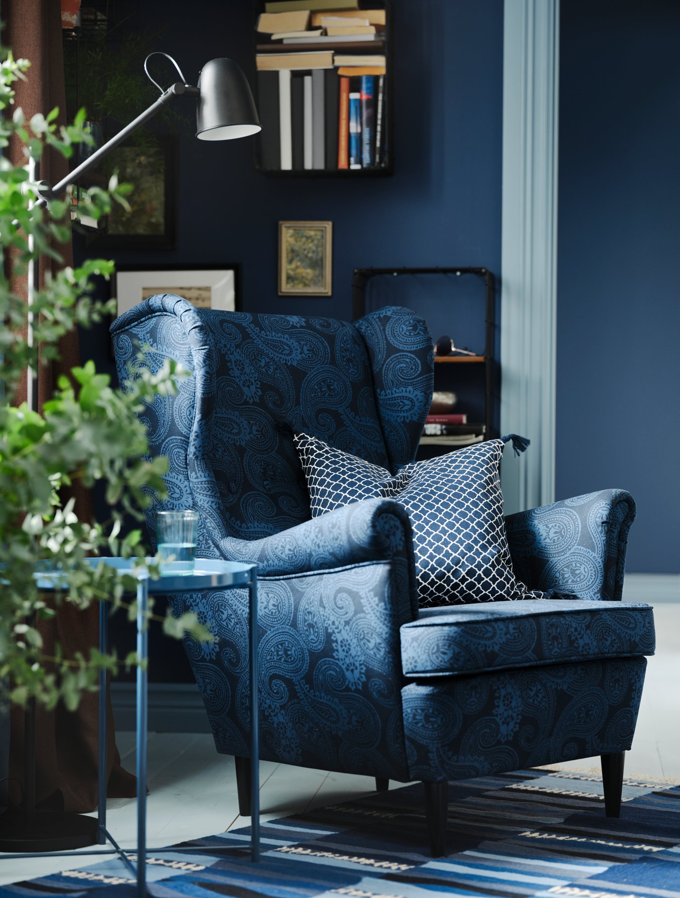 A STRANDMON wing chair with a dark blue/blue paisley pattern and a cushion with a blue/white CITRUSTRÄD cushion cover.