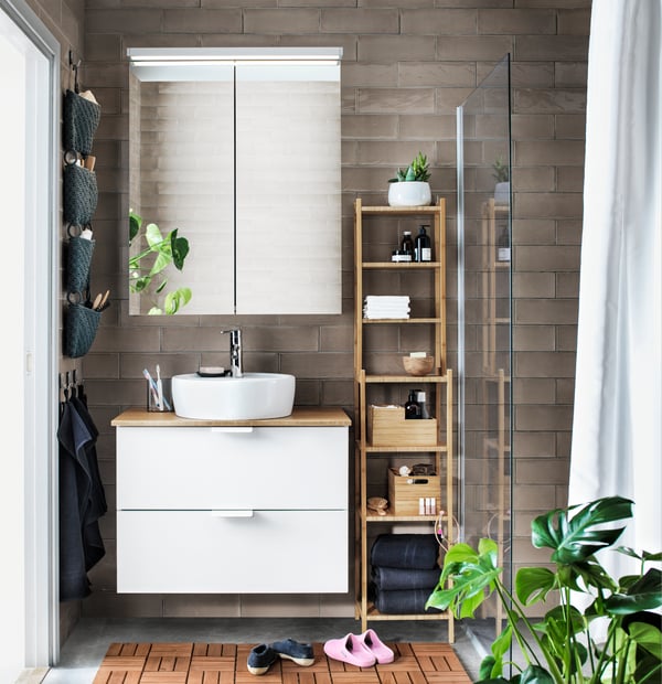 Un baño con un vanitorio de dos cajones blancos y al costado derecho un estante RÅGRUND de madera.