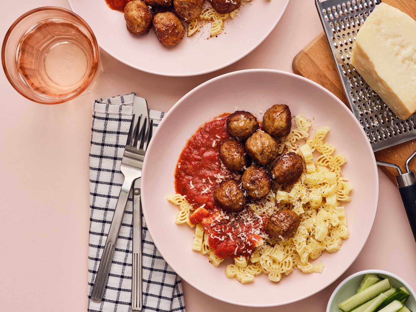 Albóndigas con pasta y salsa en un tazón de color rosa claro con cubiertos.
