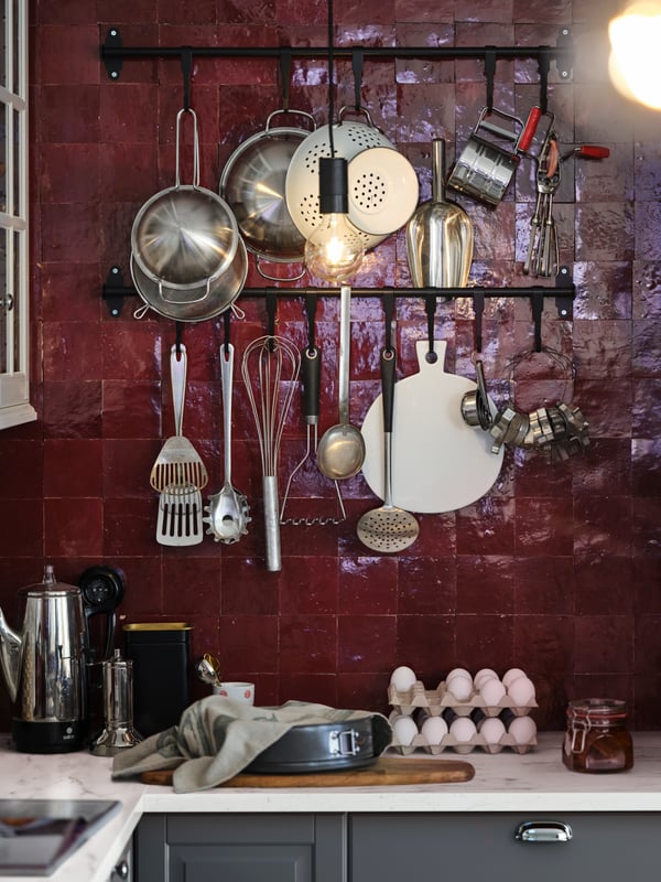 A SEKTION/MAXIMERA kitchen with black HULTARP rails holding pots and pans and a grey HEMMABAK springform pan on the worktop.