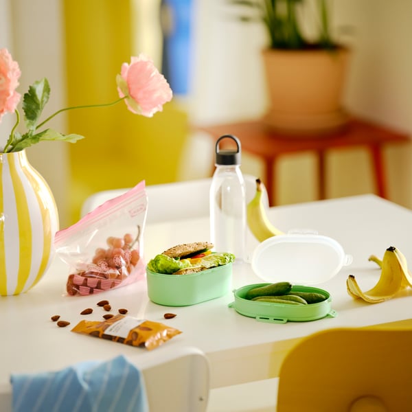 Sto s IKEA 365+ bocom za vodu tamnosive boje, UTBJUDA složivom kutijom za ručak svetlozelene boje i MUNSBIT pečenim bademima.