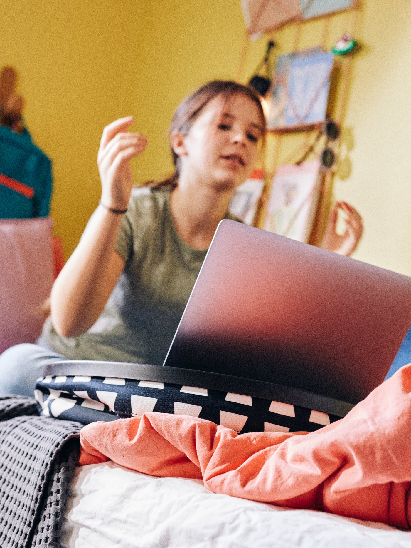 A schoolchild studies on her computer while sat on her bed, the laptop held steady by a BYLLAN laptop support.