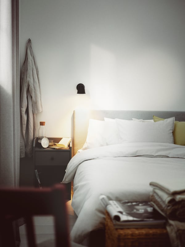 A bedroom with a Kabusa light grey upholstered bed with 4 storage boxes dressed in grey/stripe BERGPALM bed linen.