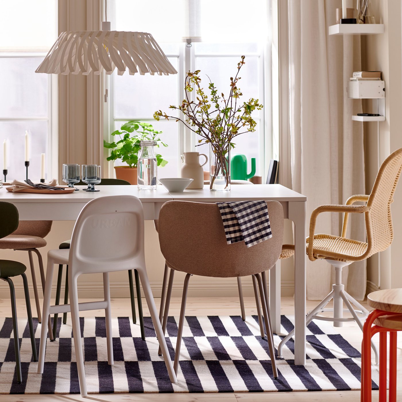 An EKEDALEN extendable table and a variety of chairs stand on a striped STOCKHOLM rug in a sunny dining room.