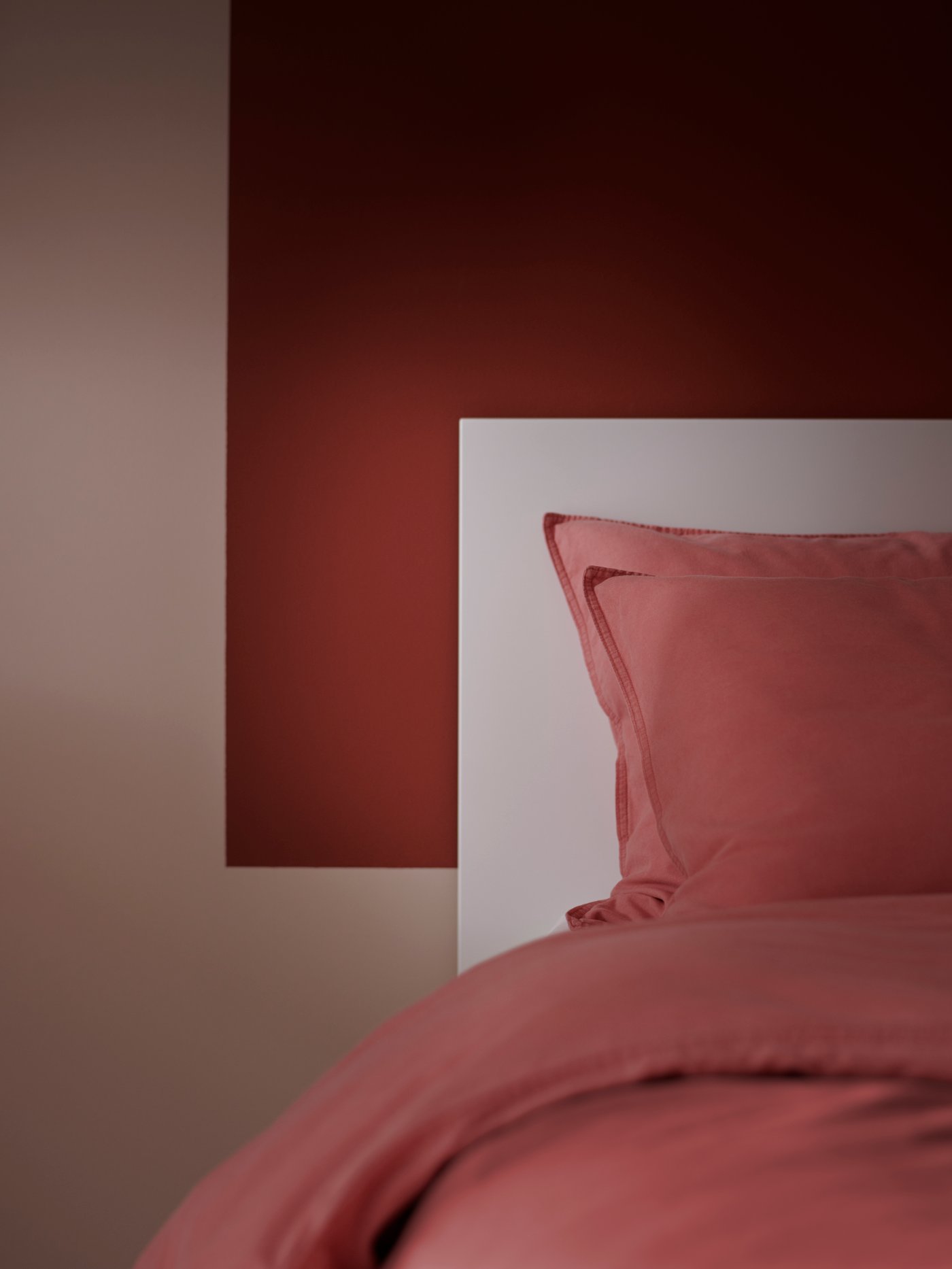 A part of a bed with light brown-red ÄNGSLILJA bed linen stands against a wall partly painted in a matching brown-red.