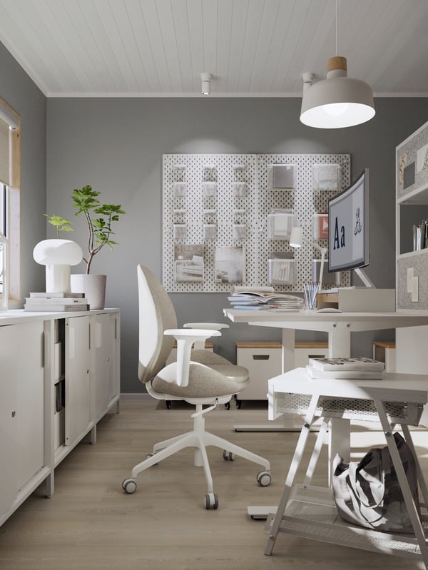 A light room in grey and white with a white TROTTEN sit-stand desk, a beige HATTEFJÄLL office chair, and office accessories.