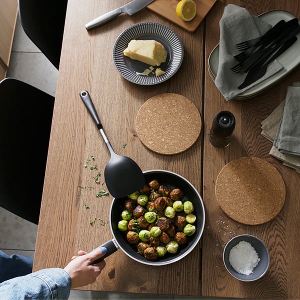 Ett köksbord i trä med en tallrik, två grytunderlägg och en stekpanna med mat i.