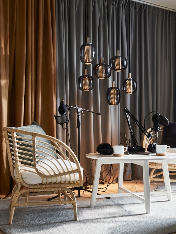 A space with recording equipment, GUNNLAUG curtains along a wall and two BUSKBO rattan armchairs by a KRAGSTA coffee table.