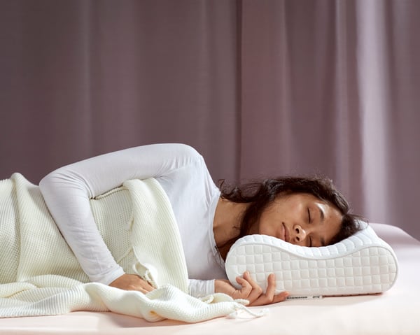 A young woman, laying on her side, is sleeping deeply on IKEA ROSENSKÄRM ergonomic pillow.