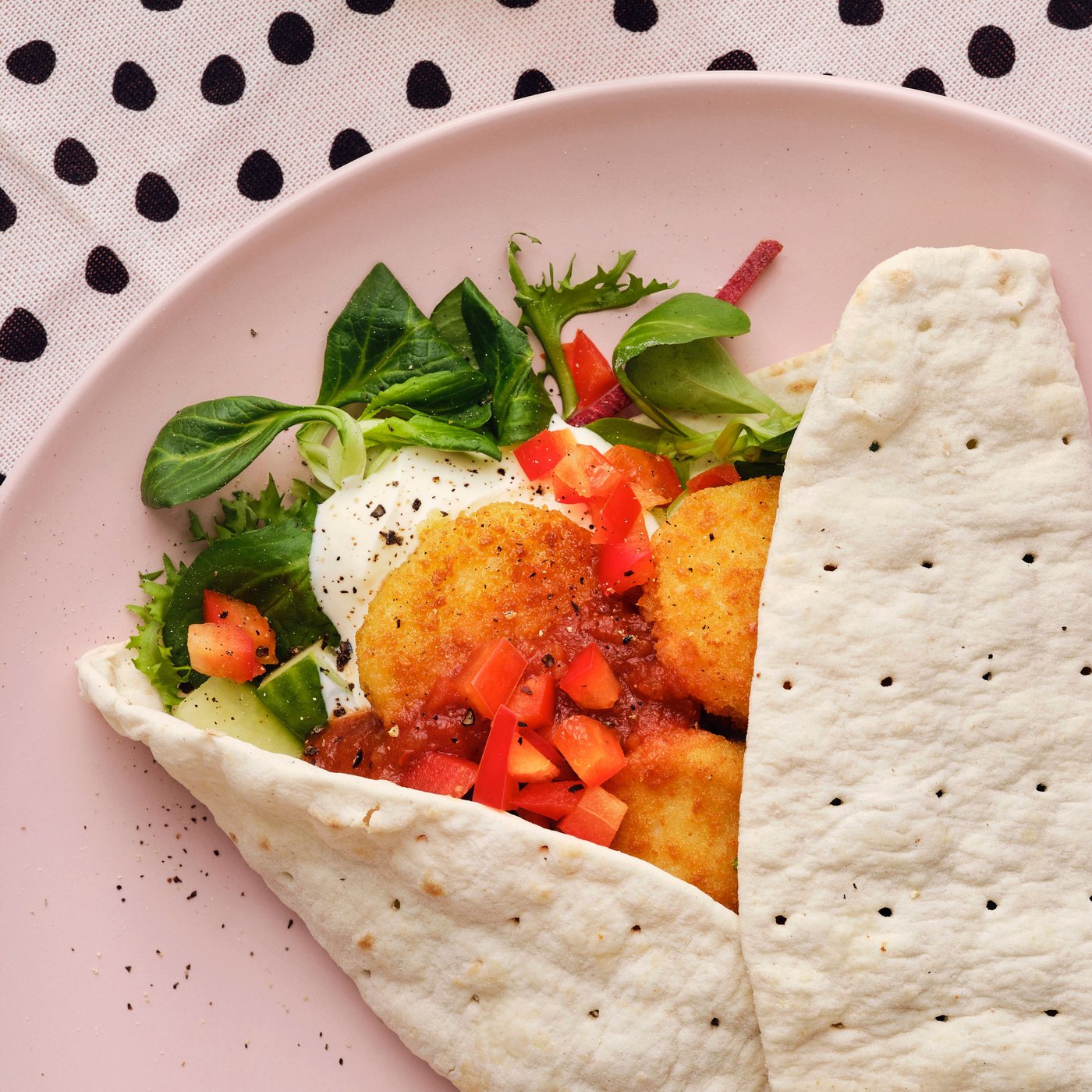 En rosa tallrik med en wrap fylld med sallad, tomater och SLAGVERK-panerade vetebaserade bitar.