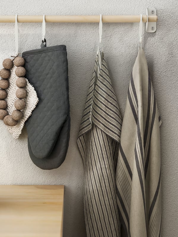 A NEREBY birch rail with striped gray-beige MARIATHERES tea towels and a dark-gray oven glove hang from white NEREBY s-hooks.