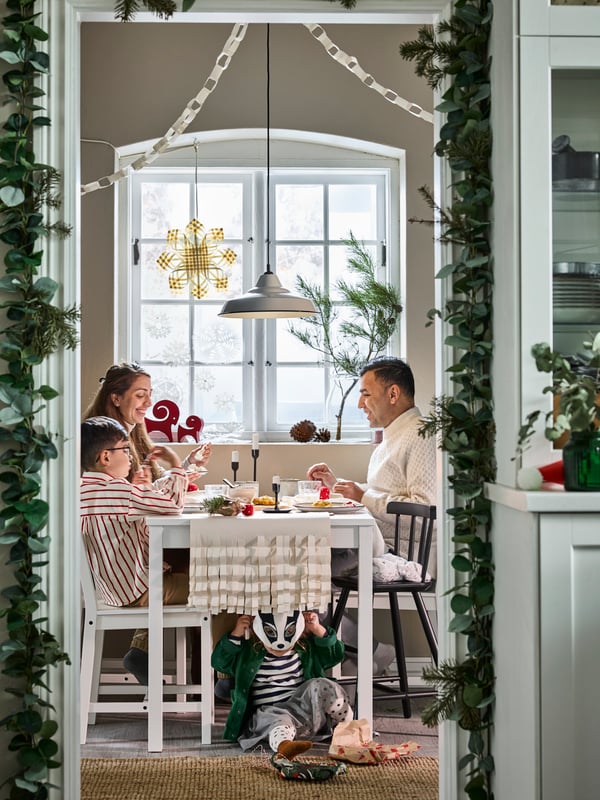Una familia reunida alrededor de una mesa blanca HAUGA de estilo escandinavo tradicional y tres sillas HAUGA, en un ambiente de comedor navideño rústico.
