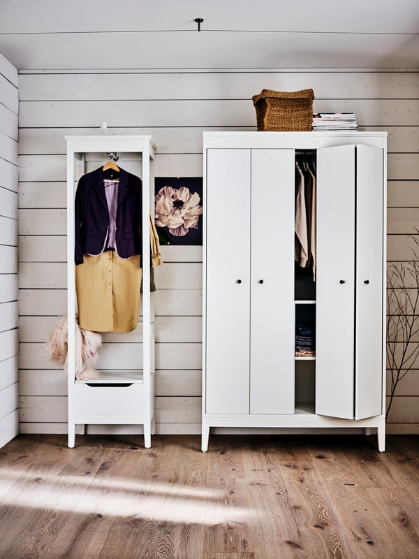 Ein weißer IDANÄS Kleiderschrank neben einem weißen offenen IDANÄS Kleiderschrank auf einem Holzboden.