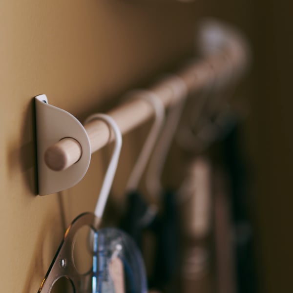 Close-up of the NEREBY rail, made of birch wood, with white NEREBY hooks hanging from it.