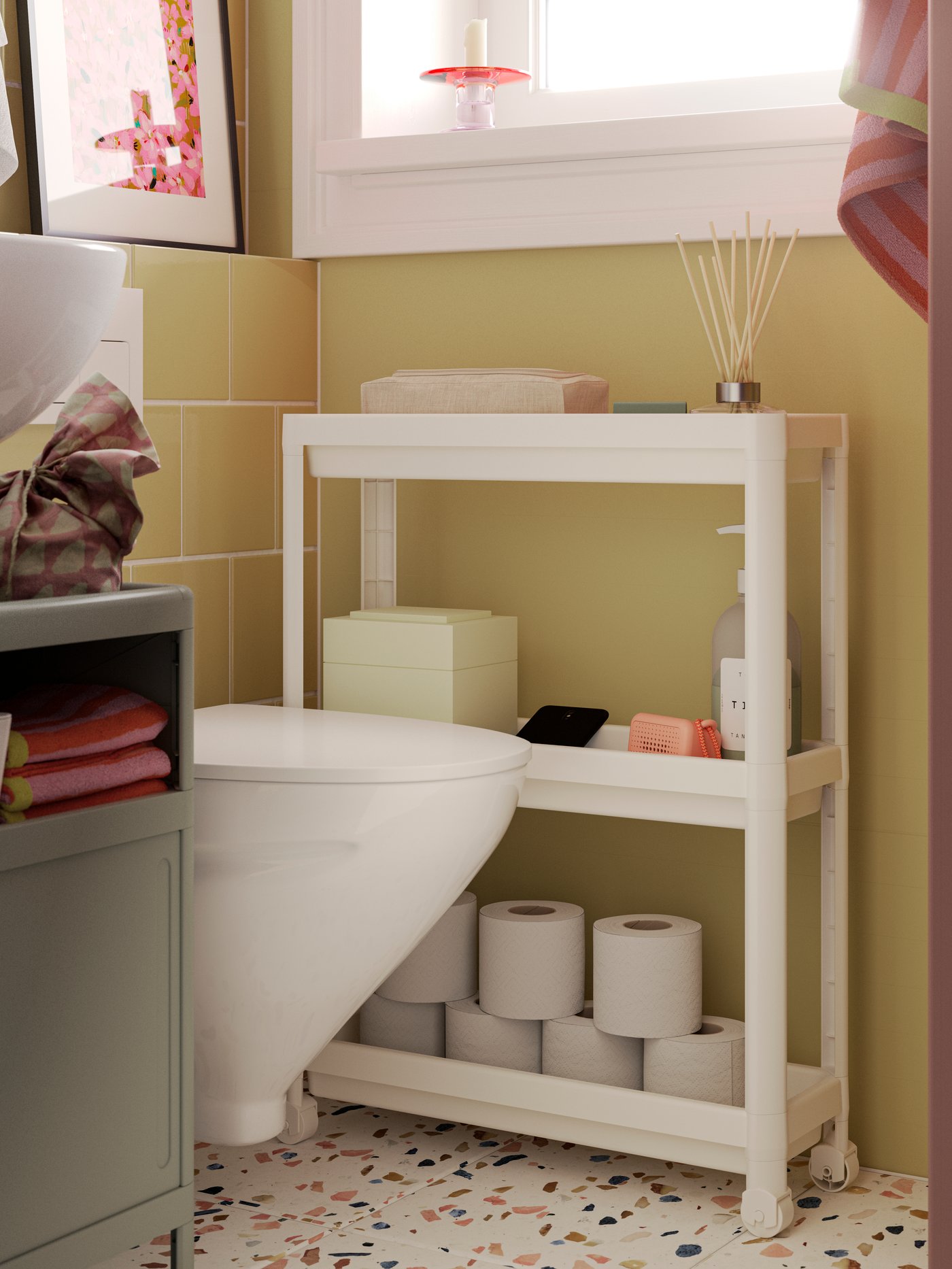 A white VESKEN trolley has toilet paper rolls on the lower shelf and other bathroom products on the other two shelves.