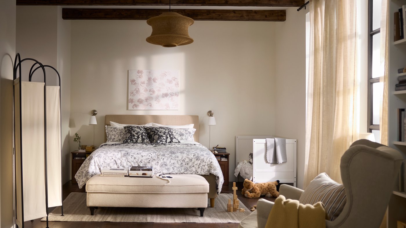 Bedroom in all beige and white with a children’s bed next to the grown-up’s bed, and an armchair in the foreground.