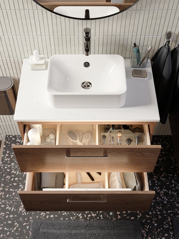 Washbasin drawers opened to reveal neatly arranged brushes in clear organisers, shampoo bottles, hairdryer and more.