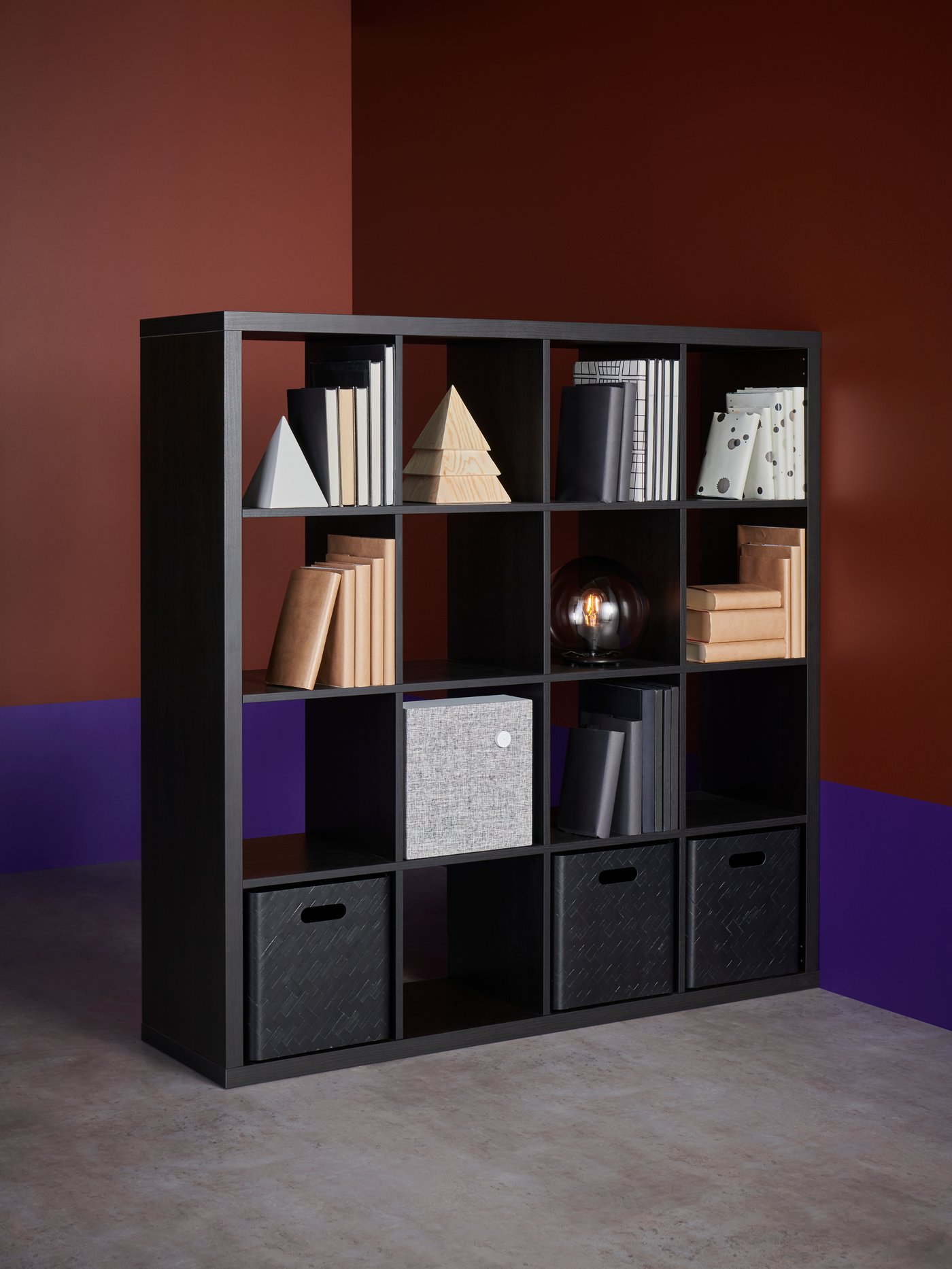 Estante KALLAX color negro con libros y artículos decorativos. En sus módulos inferiores, tiene cajas organizadoras color negro.