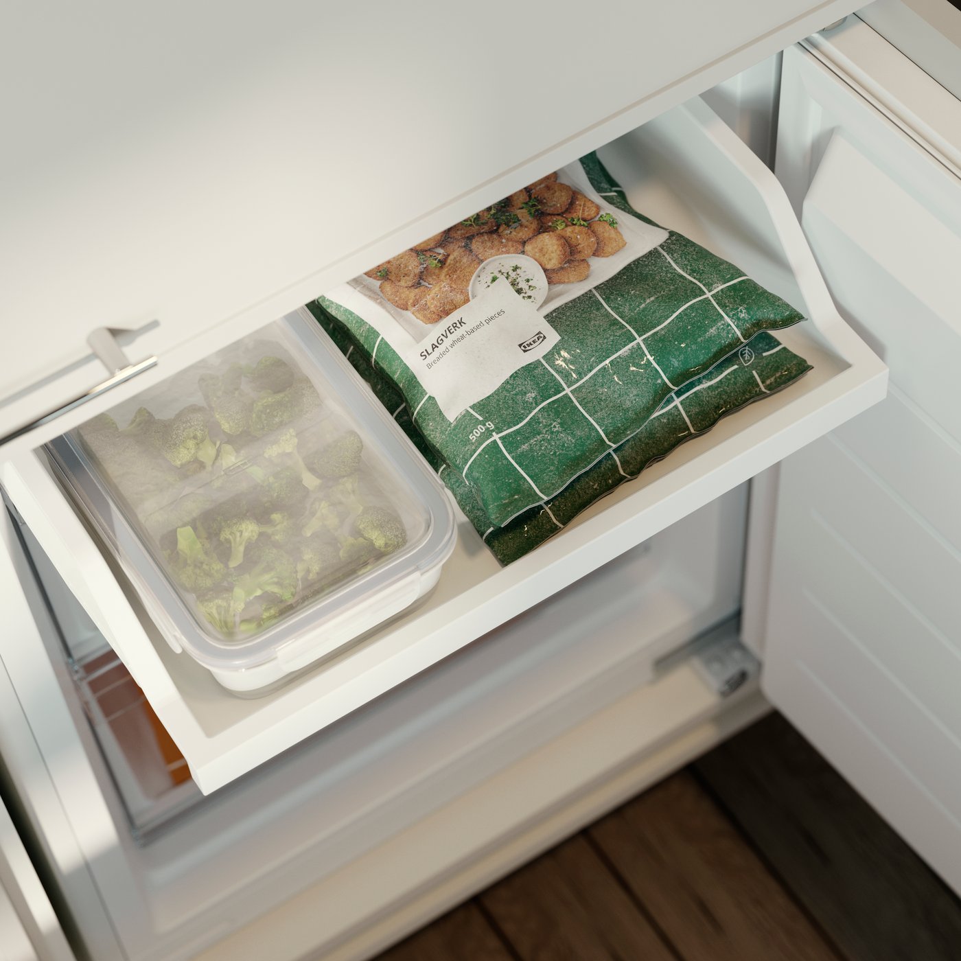 حافظة طعام IKEA 365+ بها خضراوات مخزنة في درج فريزر بجوار عبوات طعام مُجمد.  
