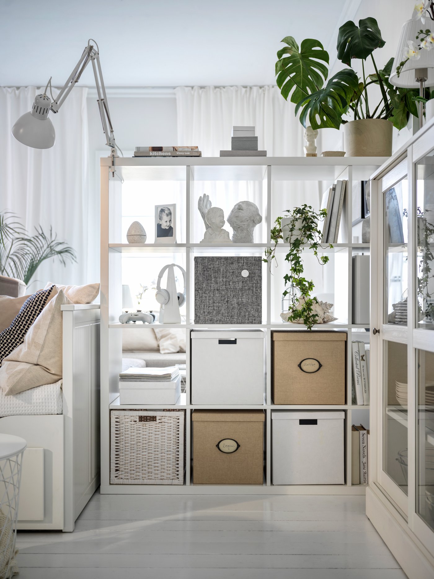 A living room with a room-dividing, white KALLAX shelving unit and a white HEMNES day-bed beside it.