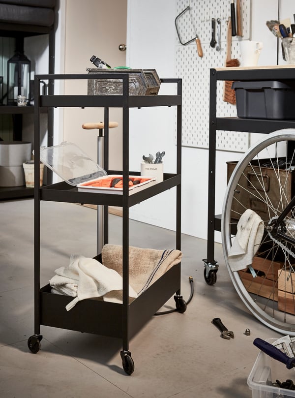 A black utility cart in a garage setting being used to store tools and other utility items.