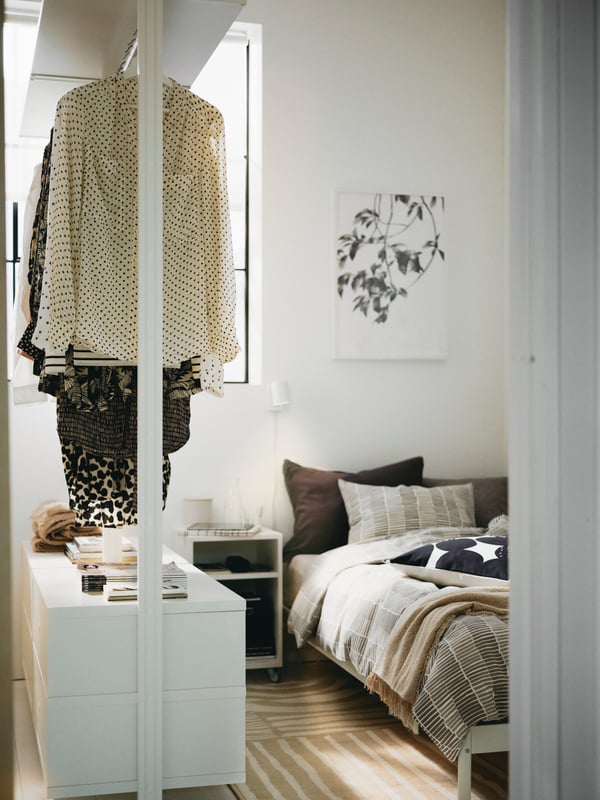 A bedroom with a white ELVARLI wardrobe combination next to a white VEVELSTAD bed dressed in white/grey bed linen.