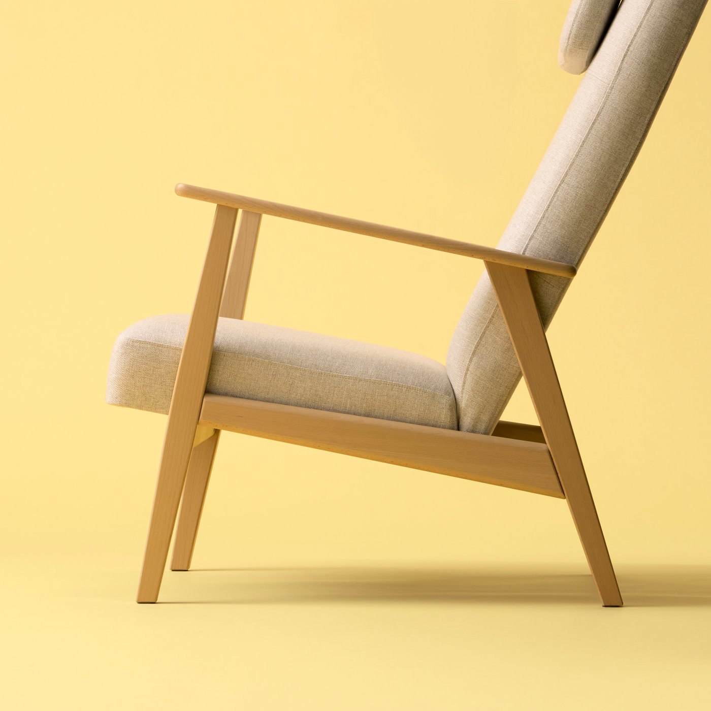 An empty EKENÄSET high-back armchair in oak-effect wood and light-beige fabric standing against a pastel-yellow background.