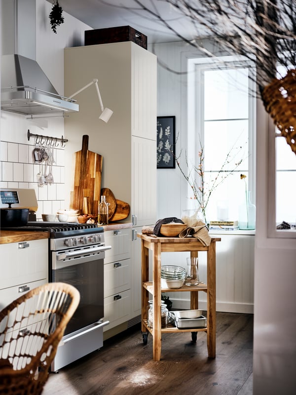Une cuisine beige de style rustique avec un comptoir en bois et des armoires blanches, et une desserte BEKVÄM au milieu de la pièce.