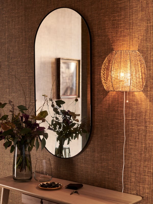 MÅNALG zidna lampa postavljena je na zid u blizini LINDBYN ogledala i iznad LISABO radnog stola na kom je cveće u vazi.