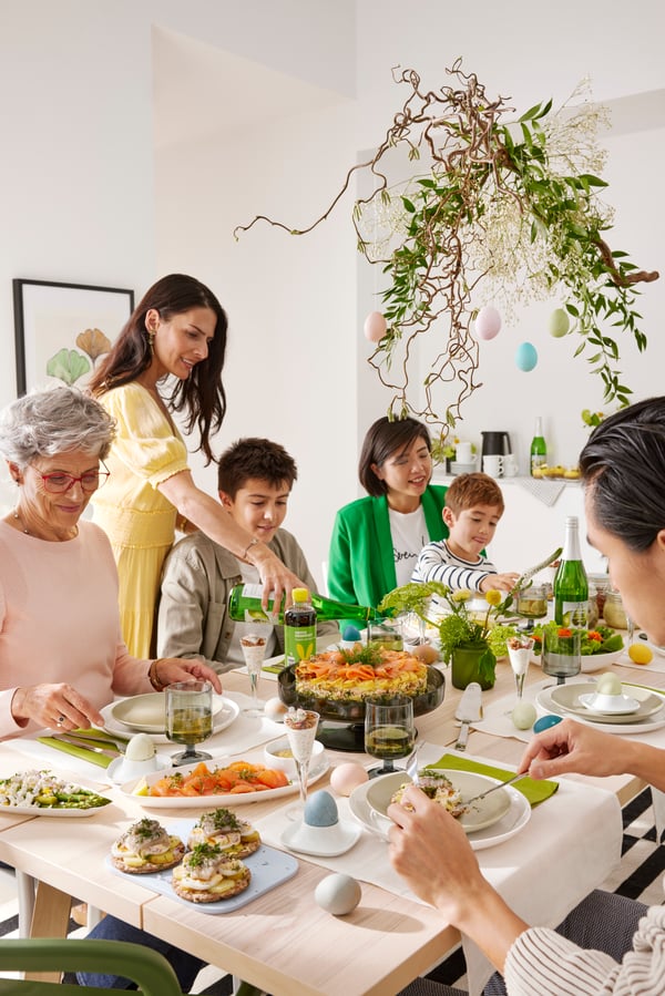 A family sitting at a dining table, gathered for an Easter meal. Salmon, eggs and crispy bread sandwiches are served.