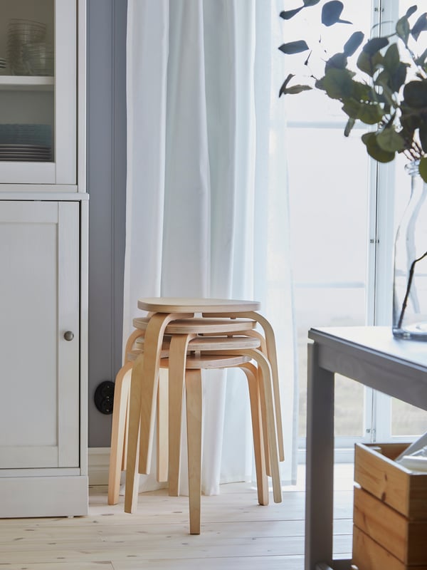 Four KYRRE stools in birch are stacked by a window, and they provide more seating by the dining table when it’s extended.