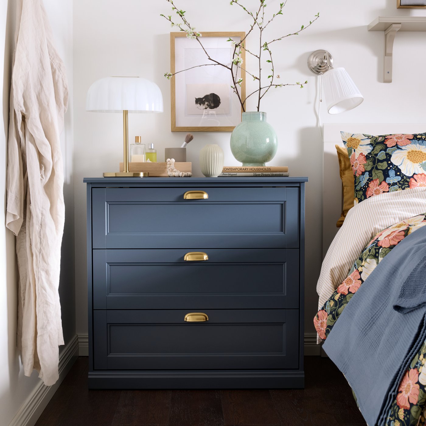 A close up of a blue FÅGELFJÄLLET chest of 3 drawers in a bedroom, styled with a lamp and decorative plants.
