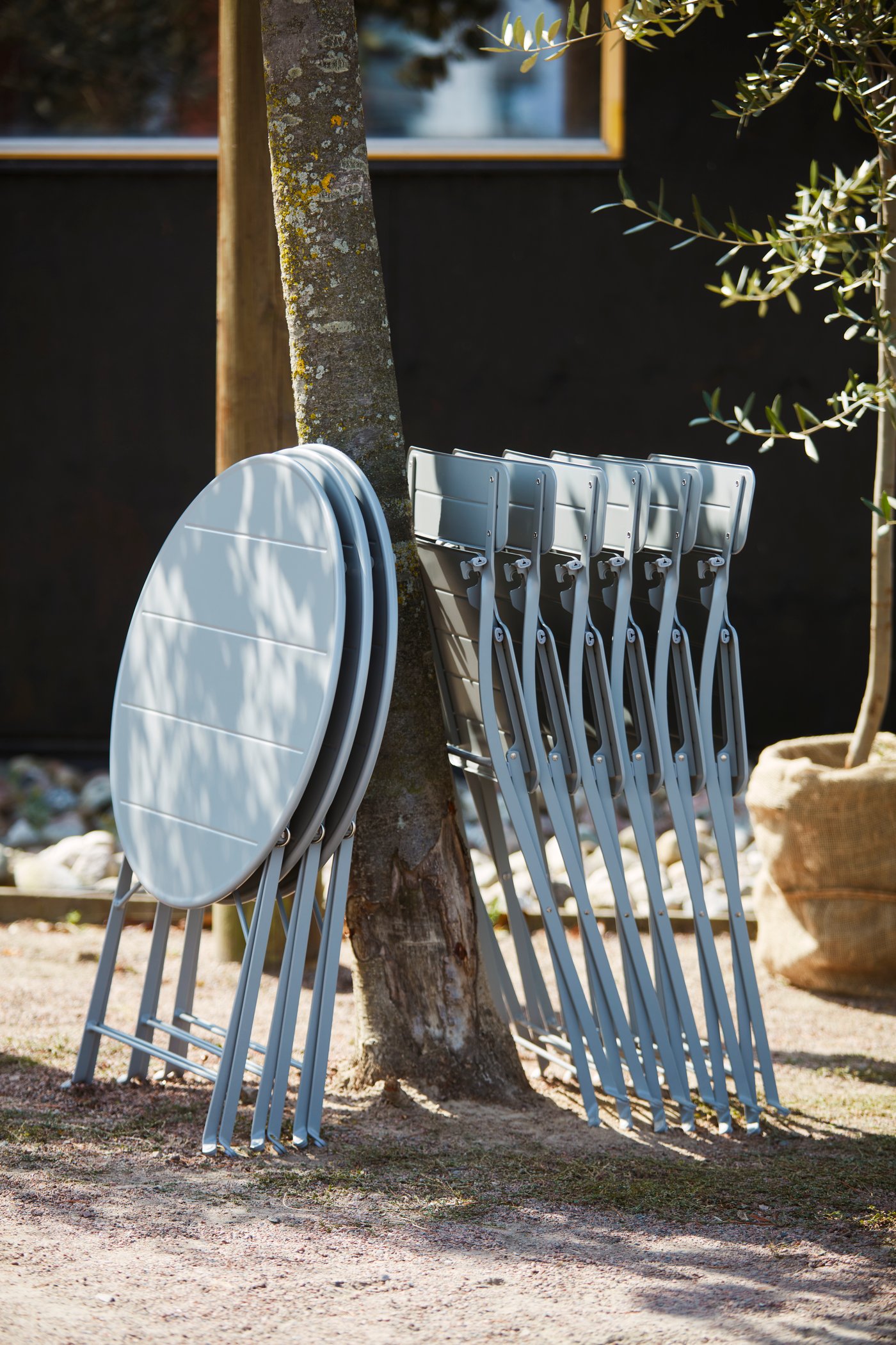 Outdoor chairs, one single and others stacked by a wall, with an outdoor table holding a coffee pot, a bag and tools.